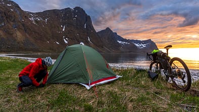 Solo woman bikepacking on a remote beach at sunset, Norway
