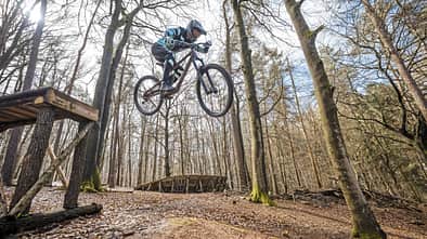Mountainbiker springt mit einem MTB über einen Holzsprung im Wald, aufgenommen in Beerfelden.