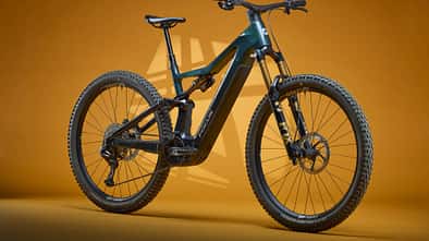Das Bild zeigt ein Focus Jam2 Next E-Mountainbike in Studioaufnahme vor orangefarbenem Hintergrund. Das vollgefederte E-MTB ist seitlich positioniert und präsentiert Details wie den integrierten Akku, die Fox-Federgabel und grobstollige Reifen.