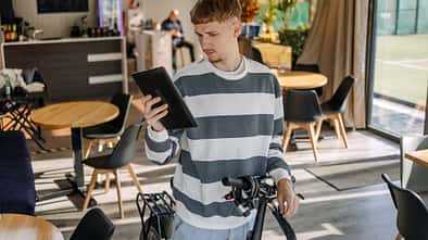 Mann, der sich im Café um sein Elektrobike kümmert und mit seinem Tablet nach etwas sucht.