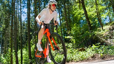Frontalansicht einer Radsportlerin auf dem orangenen Storck Fascenario.5 in Fahrt auf einer Landstraße im Wald.