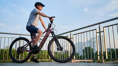 Mann fährt E-Bike auf der Stadtpromenade, Seitenansicht Radfahrer gegen blauen Himmel. 