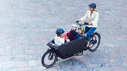 Frau fährt mit drei Kindern auf E-Lastenfahrrad. Frau fährt mit drei Kindern auf E-Lastenfahrrad.
