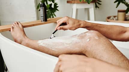 self care,home spa,shave,self love,foam,wash,bath,shaver,remove,grooming,unshave,leisure,therapy,cream,lotion,treatment,skincare,man,male,young,caucasian,body parts,lower body,guy,domestic Man shaving his leg in bathroom