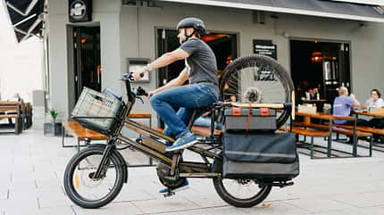 Elektrobike Test I Cargobike Moustache Lundi 20.5 I Fahrbild Mann mit MTB-Laufradsatz auf dem Heckgepäckträger