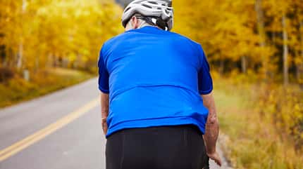 60-69 years old,aspen,fitness,male,remote,senior male Rear view of senior man riding bicycle while exercising on country road