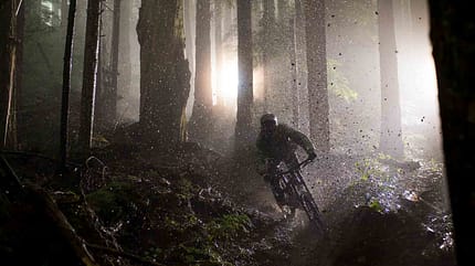 Mountainbiker fährt bei Nässe durch einen nebligen Waldtrail, aufgewirbelter Matsch im Lichtschein. Mountainbiker fährt bei Nässe durch einen nebligen Waldtrail, aufgewirbelter Matsch im Lichtschein.