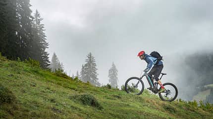 Mountainbiker fährt bergauf durch neblige, bewaldete Berglandschaft Mountainbiker fährt bergauf durch neblige, bewaldete Berglandschaft