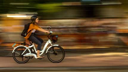 E-Bike, Stadtverkehr, urbane Mobilität, Fahrrad, Geschwindigkeit, Pendeln, Nachhaltigkeit, Abend, Bewegung, Elektromobilität, Frau, Alltag Frau fährt mit E-Bike dynamisch durch die Stadt bei Dämmerung