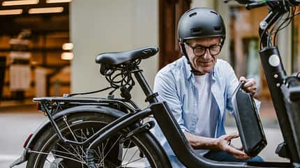 E-Bike, Akku, Wartung, Kontrolle, Elektromobilität, Fahrrad, Technik, Stadt, Alltag, Sicherheit, nachhaltige Mobilität, moderne Fahrräder, Fahrradcheck Mann überprüft E-Bike-Akku vor einem Geschäft