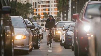 E-Bike, Pendler, Berufsverkehr, San Diego, Fahrradstreifen, urbane Mobilität, Nachhaltigkeit, Fahrradhelm, Rushhour, Verkehr, alternative Mobilität, Klimaschutz, Fahrradstadt, Stadtleben, USA Mann auf E-Bike pendelt mit Helm und Rucksack durch den Autoverkehr auf einem Fahrradstreifen in San Diego