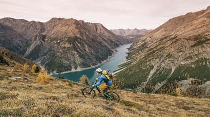 Mountain biker ascends mountainous ridge crest, valley below Mountain biker ascends mountainous ridge crest, valley below