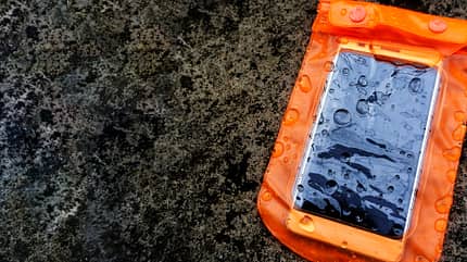 Orangefarbenes wasserdichtes Handygehäuse mit Wassertröpfchen auf Texturhintergrund. Orangefarbenes wasserdichtes Handygehäuse mit Wassertröpfchen auf Texturhintergrund.