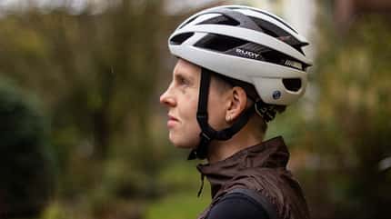 Junge Radfahrerin mit weißem Rennradhelm vor dunkelgrünem Hintergrund.