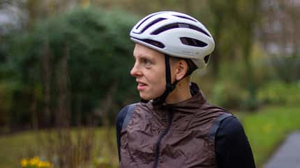 Junge Radfahrerin mit weißem Rennradhelm vor dunkelgrünem Hintergrund.