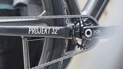 Detailaufnahme eines Fahrrad-Antriebs mit Kettenblatt, Kurbel und Kettenstrebe mit der Aufschrift 'PROJEKT 32"'. Zu sehen sind ein SRAM XX Kurbelarm und ein Wolf Tooth Kettenblatt.