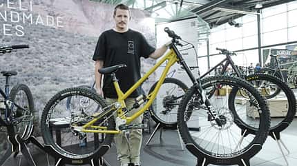 Person präsentiert ein gelbes Mountainbike auf einer Fahrradmesse, mehrere Fahrräder im Hintergrund, Indoor-Location.