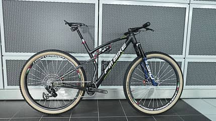 Ein modernes Mountainbike mit Carbonrahmen und Scheibenbremsen, seitlich vor einer Metallwand abgestellt.