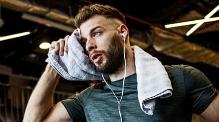 Young man running on a treadmill wiping his sweat with towel