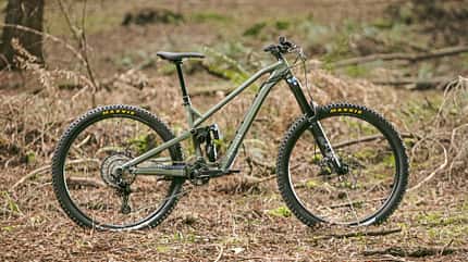 Vollgefedertes Mountainbike mit Maxxis-Reifen im Wald, Seitenansicht, Modell und Marke nicht aus Dateiname ersichtlich.
