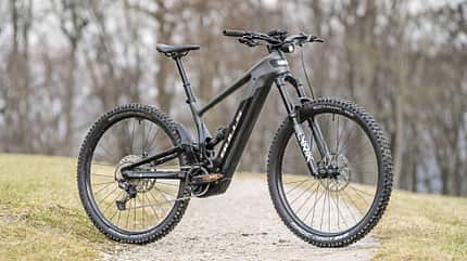 E-Mountainbike der Marke Bulls mit Vollfederung auf einem Schotterweg, Modelljahr vermutlich 2026, aufgenommen im Außenbereich.