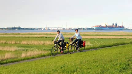 Pärchen radelt am Deich, Containerschiff im Hintergrund 
