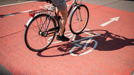 Schatten eines unkenntlichen Radfahrers, der mit dem Fahrrad auf dem Radweg fährt.
