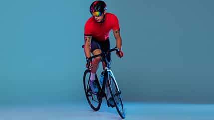 Studio shot of professional cyclist in red sports uniform, goggles and a helmet on a blue background. Concept of active life, rest, travel, energy, sport