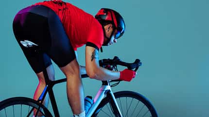 Studio shot of professional cyclist in red sports uniform, goggles and a helmet on a blue background. Concept of active life, rest, travel, energy, sport