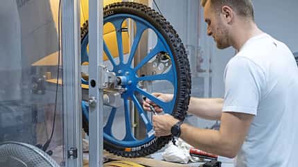 Ein Techniker führt einen Dichtmilchtest an einem Schwalbe-Fahrradreifen für das Modelljahr 2025 durch. Das Laufrad ist in einer Prüfmaschine eingespannt.