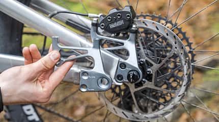 Detailaufnahme eines Mountainbike-Hinterbaus mit Ausfallende, Scheibenbremse und Hand, die ein Bauteil hält. Die Aufnahme stammt vom Event MTB Beerfelden und zeigt ein eignerframes-Bike.