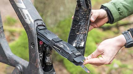 Detailaufnahme eines Mountainbike-Rahmens mit geöffnetem Unterrohrfach, in dem Werkzeug und Ersatzteile verstaut sind. Zu sehen ist ein FOX-Federbein und ein Syncros-Multitool-System.