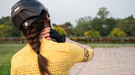 Rear view of female cyclist having neck pain from riding a bike long time. Rear view of female cyclist having neck pain from riding a bike long time.