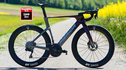 Das Merida Reacto One mit Roadbike Testsiegel "Tipp Aero" in seiner rot-grauen Lackierung auf einer asphaltierten Straße. 