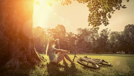 Woman sitting under sun near her bicycle in the park