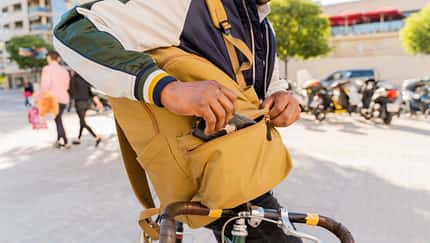 Casual businessman with bicycle taking cell phone out of backpack in the city, Barcelona, Spain