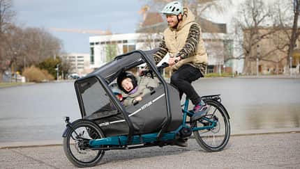Mann mit 2 Kindern im Kindersitz auf der Front des Kettler Cargobikes