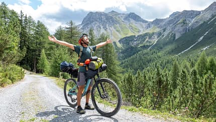Man bikepacking, he stops and embraces nature arms wide open