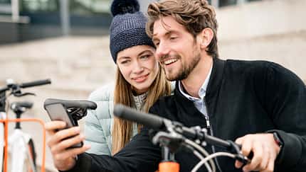 Smiling couple with bicycles and cell phone in the city