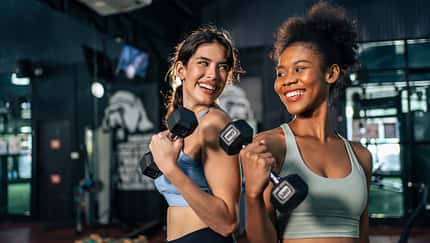 Latino and African sport woman exercising and build muscle in stadium. Active strong beautiful fit athlete girls in sportswear workout lifting weight dumbbell for arm and health care at fitness club.