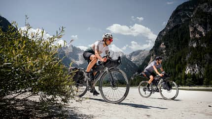 A female and a male cyclist on a gravel road with mountains in the background
