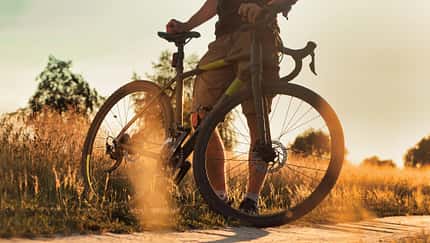 Cyclist with bicycle on a dirt trail at the sunset in the field.