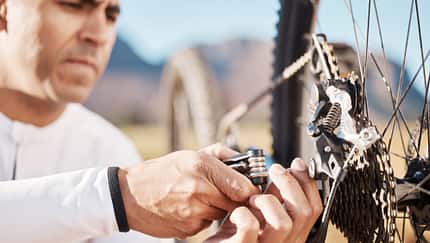Hands, repair and wheel with man and bicycle for sports, wellness and fitness training. Insurance, safety and tire change with cyclist fixing mountain bike on trail for broken, puncture and check