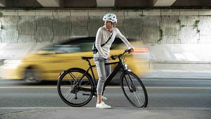 A woman riding a battery-powered commuter e-bike through Vancouver, passing iconic locations like Gastown and Stanley Park, with a view of the downtown city skyline. A woman riding a battery-powered commuter e-bike through Vancouver, passing iconic locations like Gastown and Stanley Park, with a view of the downtown city skyline.