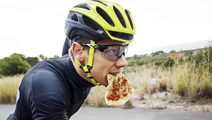 Man eating pizza while cycling on street against clear sky