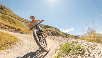 Mountainbiker fährt dynamisch auf Schotterweg durch sonnige Hügellandschaft