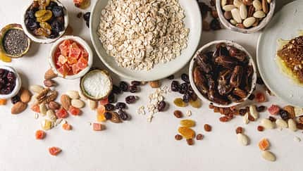 Variety of dried fruits. nuts. honey and oat flakes in ceramic bowls for cooking homemade healthy breakfast muesli or granola energy bars over white texture background. Flat lay. space.