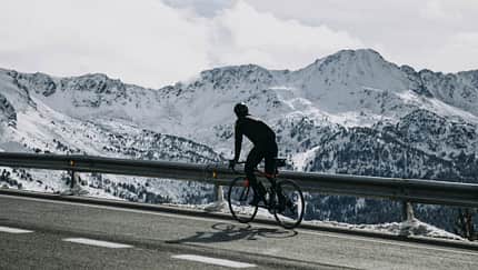 Andorra, cyclist on mountain road with snowy mountains in the background