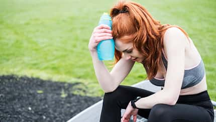 Young woman with long red hair wearing sportswear, exercising outdoors.