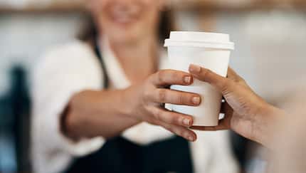 Beschnittene Aufnahme eines Baristas, der einem Kunden in einem Café einen Becher Kaffee reicht